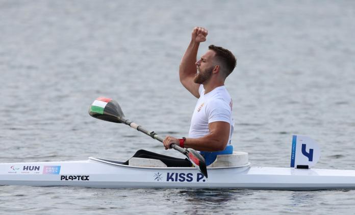 A photo taken from the side of a male Para canoe athlete pumping his right fist in the air after finishing his race